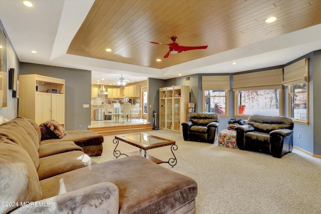 carpeted living room with a raised ceiling, ceiling fan, and wooden ceiling