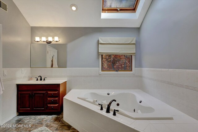 bathroom featuring tiled tub, vanity, and a skylight