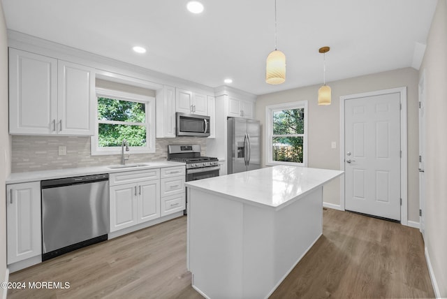 kitchen with stainless steel appliances, sink, white cabinetry, light hardwood / wood-style flooring, and decorative light fixtures