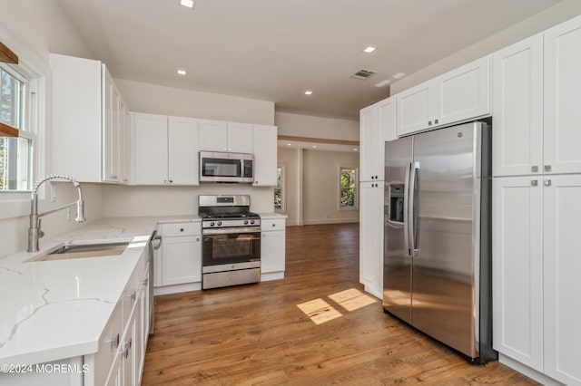 kitchen with white cabinetry, stainless steel appliances, sink, and light hardwood / wood-style flooring