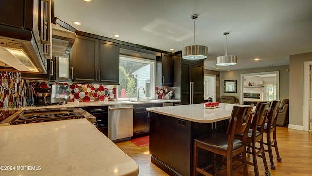 kitchen with appliances with stainless steel finishes, sink, decorative light fixtures, light hardwood / wood-style flooring, and a kitchen island