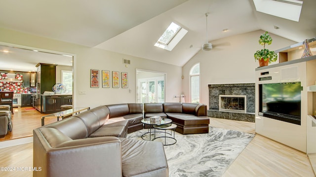 living room with a skylight, ceiling fan, a fireplace, and light hardwood / wood-style floors