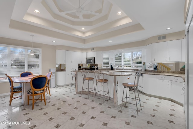 kitchen with white cabinetry, stone countertops, a raised ceiling, and a breakfast bar area