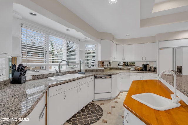 kitchen with white cabinets, sink, white dishwasher, and light stone counters