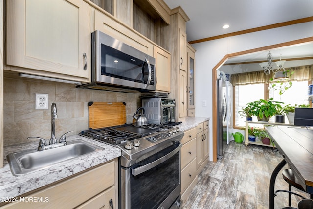 kitchen with stainless steel appliances, sink, crown molding, a notable chandelier, and light hardwood / wood-style floors