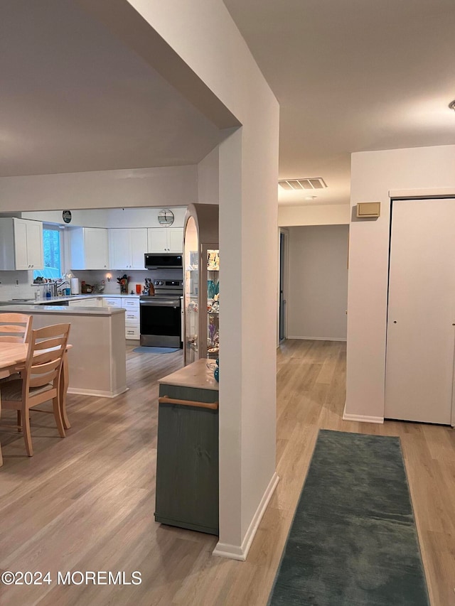 kitchen with ventilation hood, light hardwood / wood-style flooring, white cabinetry, and electric range