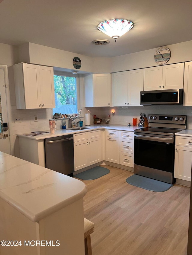 kitchen featuring tasteful backsplash, white cabinetry, light hardwood / wood-style flooring, sink, and stainless steel appliances