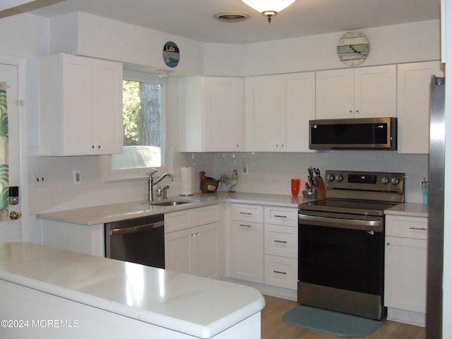 kitchen featuring tasteful backsplash, appliances with stainless steel finishes, sink, white cabinetry, and light hardwood / wood-style floors