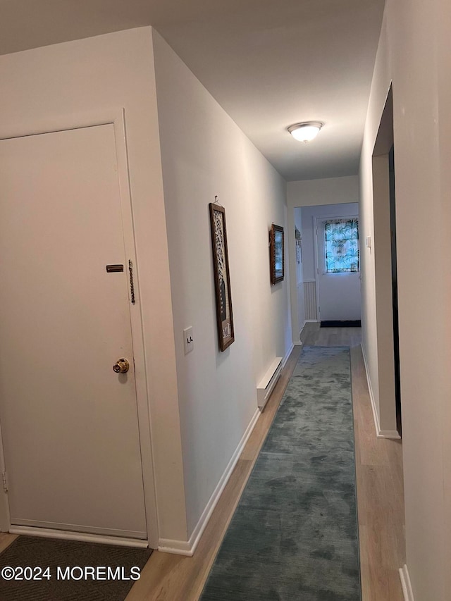 corridor with a baseboard heating unit and hardwood / wood-style flooring