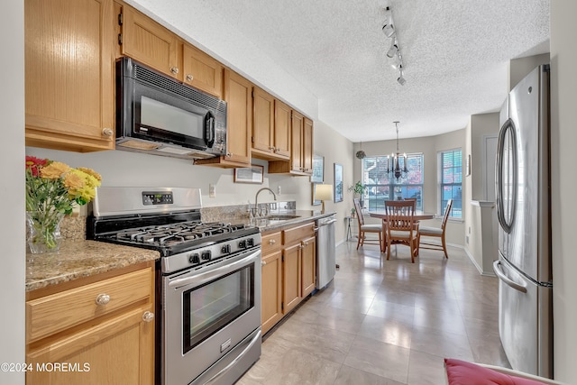 kitchen with appliances with stainless steel finishes, sink, rail lighting, pendant lighting, and a notable chandelier