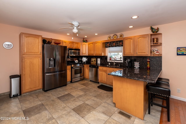 kitchen with ceiling fan, dark stone countertops, a kitchen bar, kitchen peninsula, and stainless steel appliances