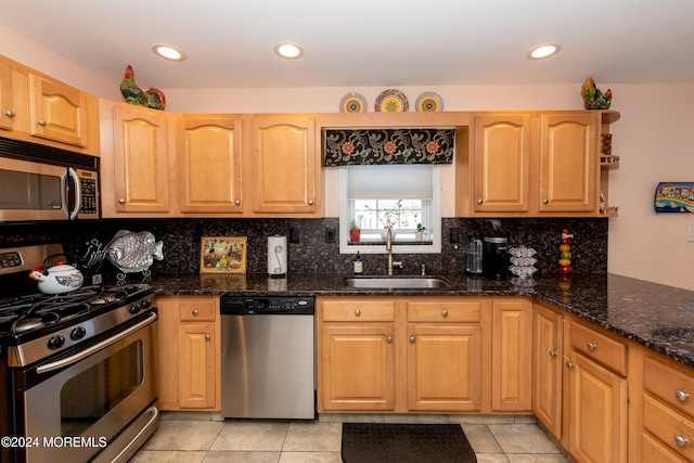 kitchen featuring appliances with stainless steel finishes, tasteful backsplash, sink, dark stone countertops, and light tile patterned flooring