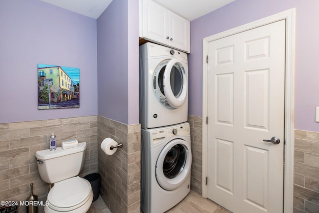 laundry area with light tile patterned floors, tile walls, and stacked washer and clothes dryer