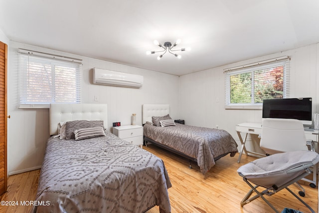 bedroom with light hardwood / wood-style floors, a notable chandelier, and a wall mounted AC