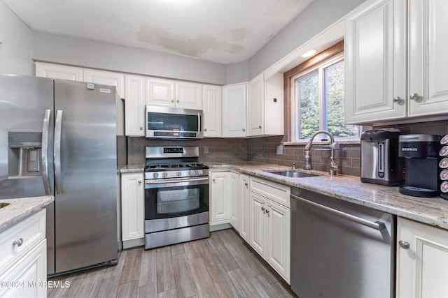 kitchen featuring appliances with stainless steel finishes, sink, white cabinetry, light stone counters, and light hardwood / wood-style flooring