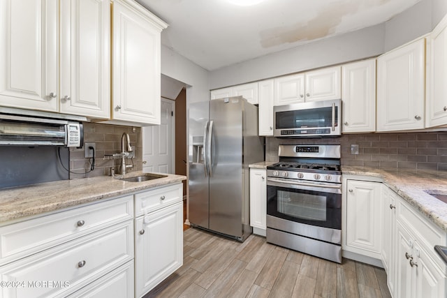 kitchen featuring appliances with stainless steel finishes, sink, white cabinetry, decorative backsplash, and light hardwood / wood-style flooring