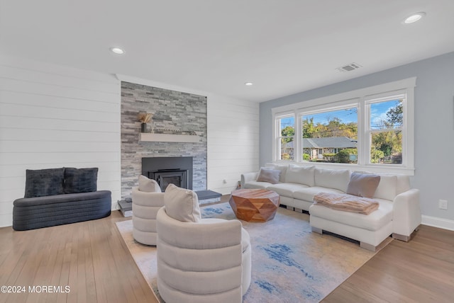 living room with light hardwood / wood-style floors, a stone fireplace, and wooden walls