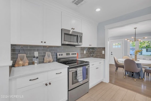 kitchen featuring white cabinetry, stainless steel appliances, a notable chandelier, and light hardwood / wood-style flooring