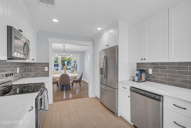 kitchen featuring white cabinetry, stainless steel appliances, a notable chandelier, and backsplash