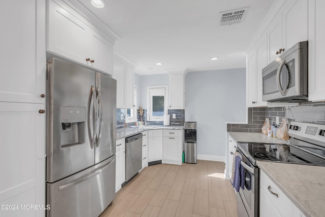 kitchen with light hardwood / wood-style flooring, backsplash, white cabinets, and stainless steel appliances