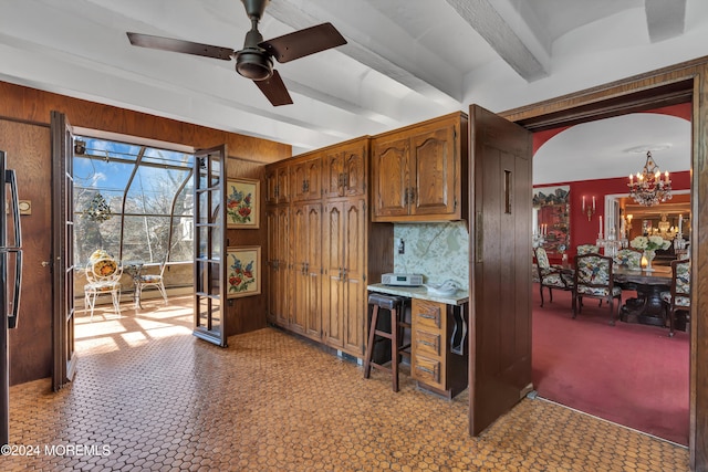 kitchen with ceiling fan with notable chandelier, refrigerator, wood walls, backsplash, and beam ceiling