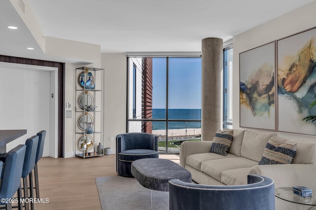 living room with visible vents, a water view, light wood-style floors, recessed lighting, and expansive windows