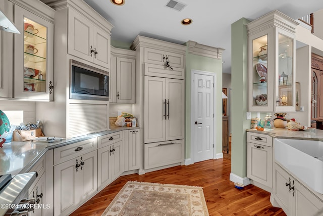 kitchen with white cabinets, light stone countertops, light hardwood / wood-style flooring, and stainless steel microwave