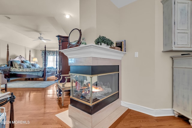 bedroom with hardwood / wood-style floors, vaulted ceiling, and a multi sided fireplace