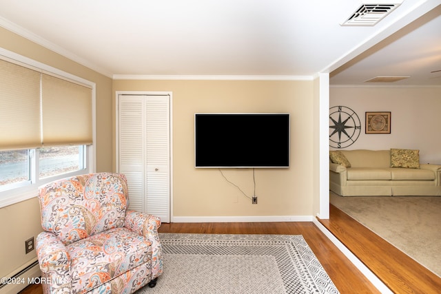 living area with hardwood / wood-style floors, a baseboard radiator, and ornamental molding