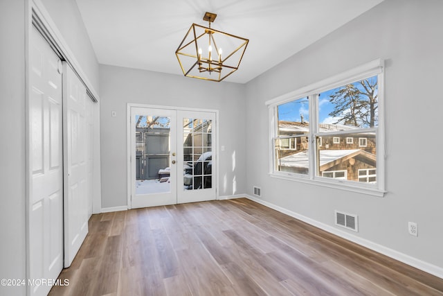 unfurnished dining area featuring french doors, hardwood / wood-style floors, and an inviting chandelier