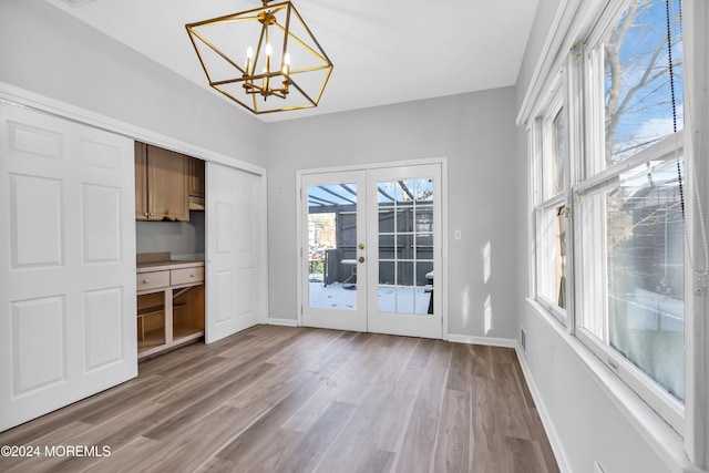 unfurnished dining area with wood-type flooring, a chandelier, and french doors