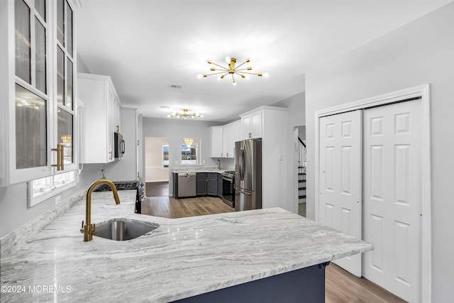 kitchen featuring white cabinetry, sink, appliances with stainless steel finishes, hardwood / wood-style floors, and a notable chandelier