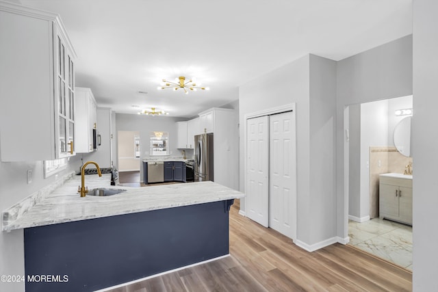 kitchen featuring stainless steel appliances, white cabinets, kitchen peninsula, sink, and light hardwood / wood-style flooring