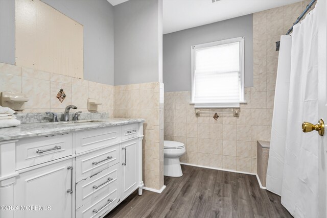 bathroom with wood-type flooring, vanity, toilet, and tile walls