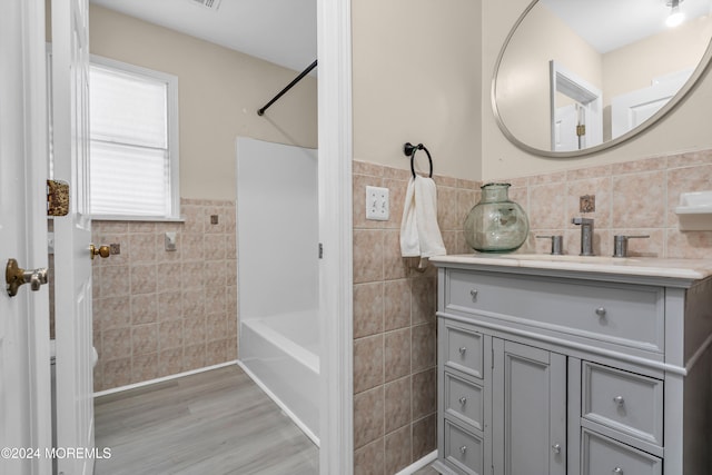 bathroom featuring tile walls, hardwood / wood-style floors, vanity, and washtub / shower combination