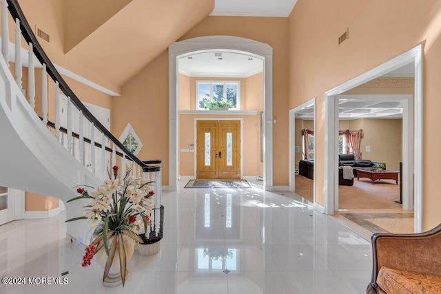 entryway featuring a towering ceiling, light tile patterned floors, and ornamental molding