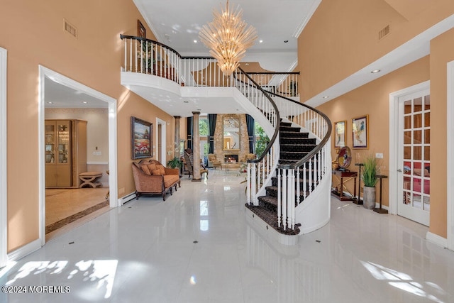 entrance foyer with a towering ceiling, a chandelier, a stone fireplace, and crown molding