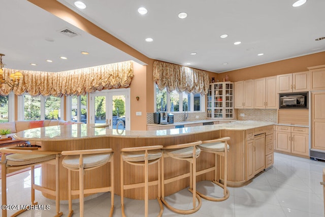 kitchen with light tile patterned flooring, a kitchen breakfast bar, a center island, black microwave, and decorative backsplash