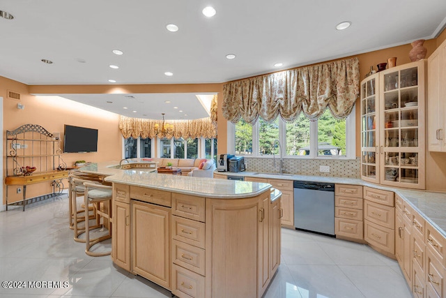 kitchen featuring a breakfast bar, light brown cabinetry, backsplash, stainless steel dishwasher, and a kitchen island