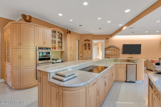 kitchen featuring light brown cabinets, black electric stovetop, a center island with sink, and light stone counters