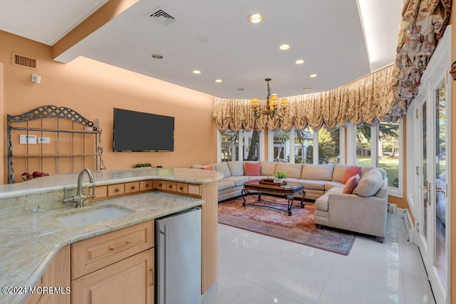 kitchen with stainless steel fridge, light tile patterned floors, light brown cabinetry, sink, and a chandelier