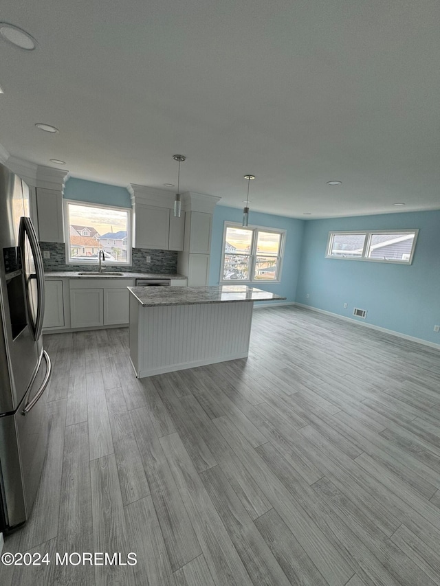 kitchen featuring a wealth of natural light, light wood-type flooring, hanging light fixtures, and stainless steel fridge with ice dispenser