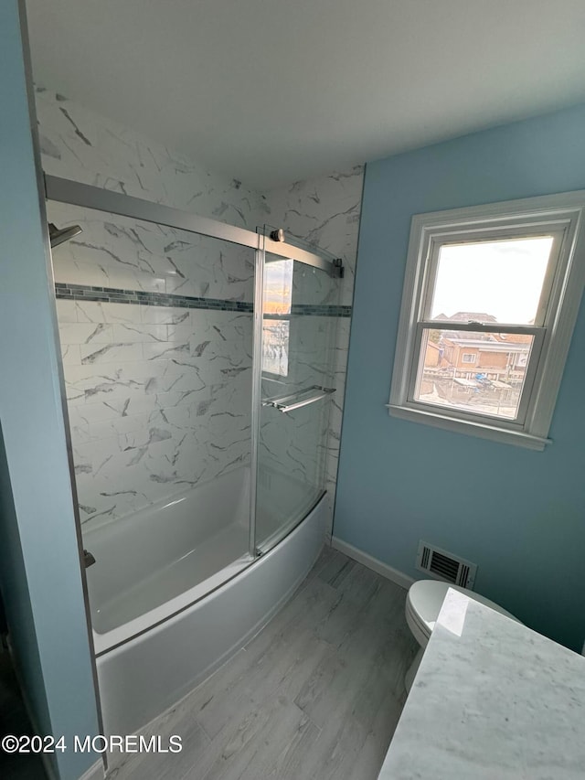 bathroom with toilet, wood-type flooring, and shower / bath combination with glass door