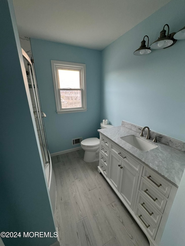 bathroom with hardwood / wood-style floors, walk in shower, vanity, and toilet