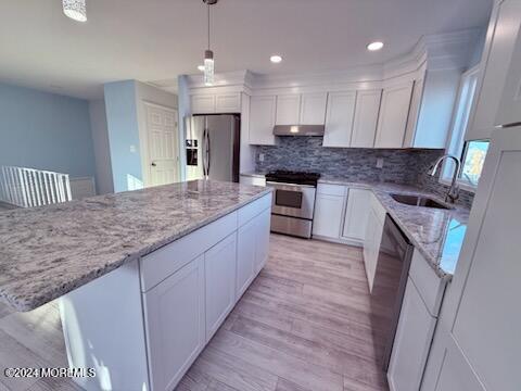 kitchen with appliances with stainless steel finishes, decorative light fixtures, sink, light hardwood / wood-style floors, and white cabinets