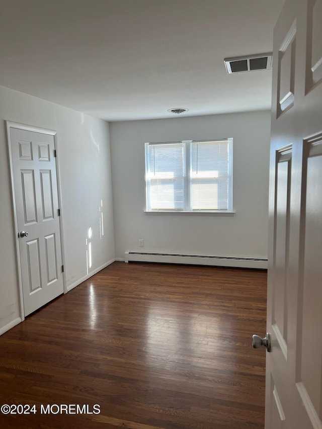 empty room featuring dark wood-type flooring and a baseboard heating unit