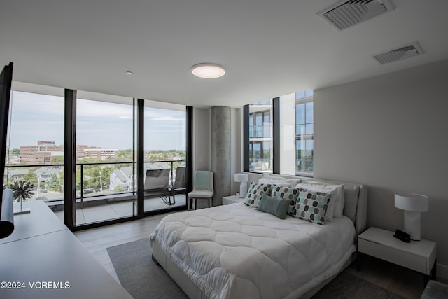 bedroom with light hardwood / wood-style floors, access to exterior, and a wall of windows