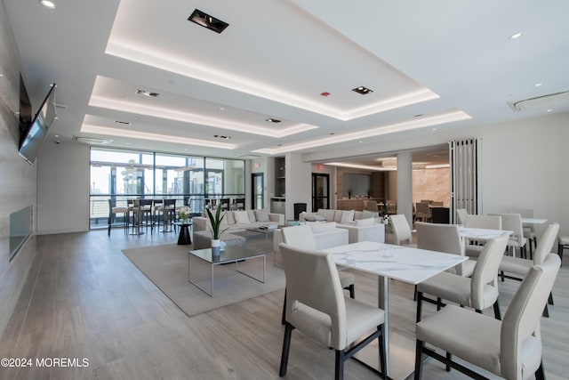 dining space with a raised ceiling, expansive windows, and light wood-type flooring