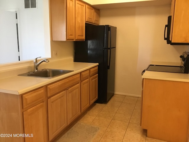 kitchen featuring range, light tile patterned floors, black fridge, and sink