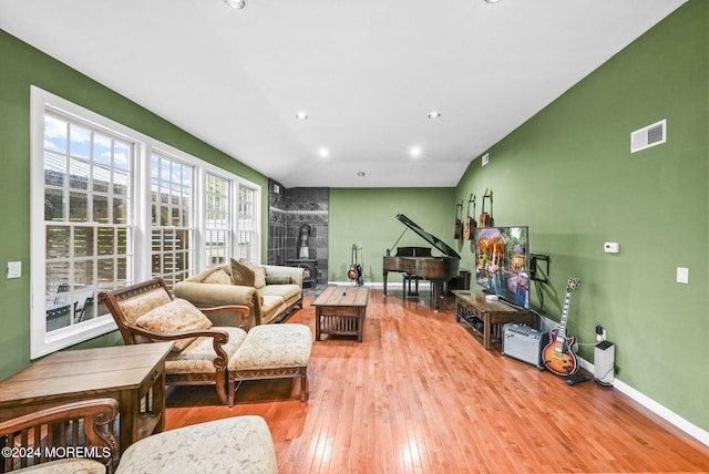 living room with wood-type flooring, vaulted ceiling, and a wood stove